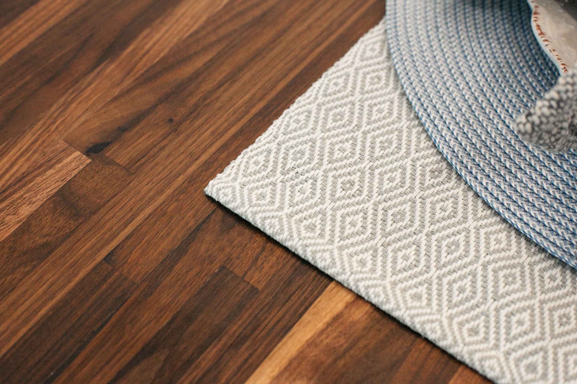 Close-up of a wooden floor with a patterned rug and a blue woven mat.